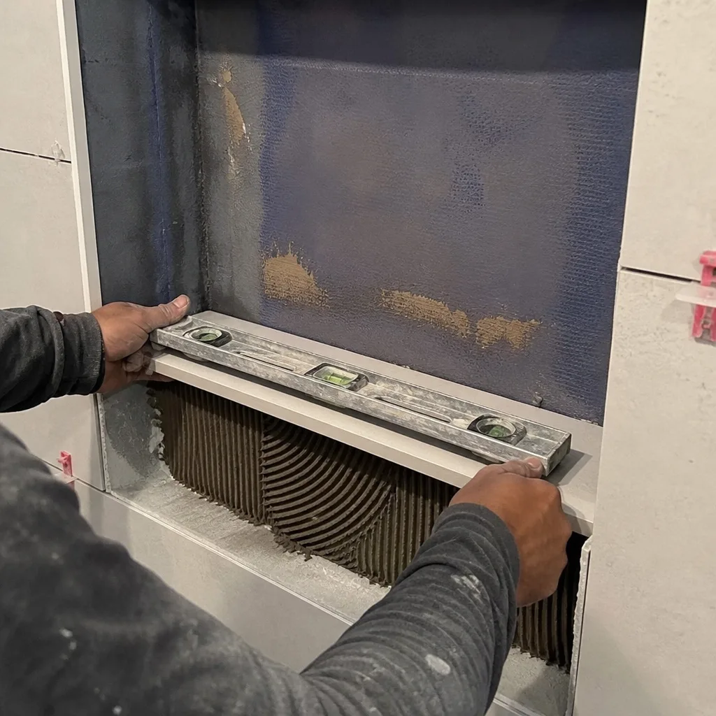 Worker using a level to install a bathroom tile niche shelf